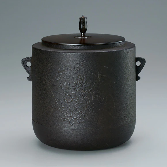 Cylindrical tea ceremony kettle with flowering plant design.