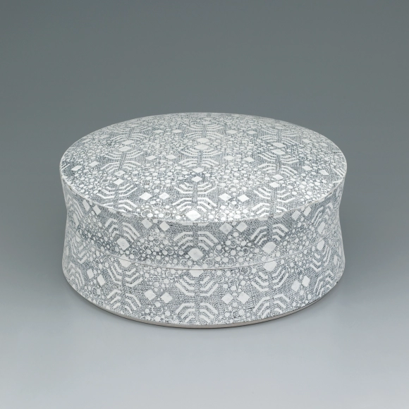 Circular box with connected minute patterns in cut paper stencil.